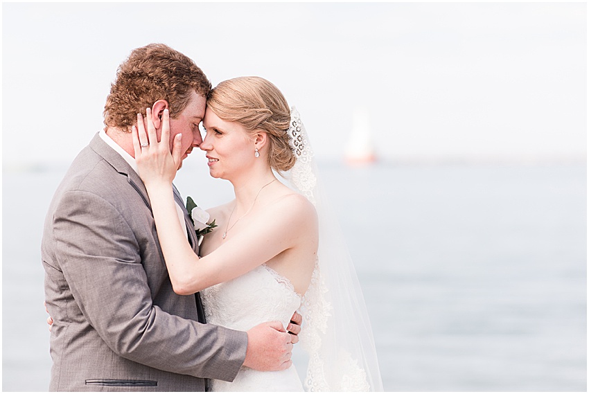 Bride and groom nose to nose with the bride’s left hand holding chin of groom. Lighthouse and Lake Michigan can be seen in the blurred background. 